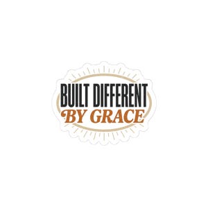 May include: A white sticker with the text "BUILT DIFFERENT" in black, arched over "BY GRACE" in brown. The text is inside a cream-colored oval with a scalloped edge and radiating lines.