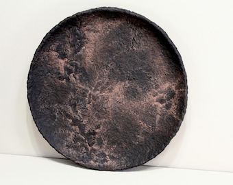 May include: A round, textured decorative tray with a dark brown and reddish-brown color scheme. The tray has a rough, uneven surface and a raised edge. The tray is likely made of ceramic or a similar material.