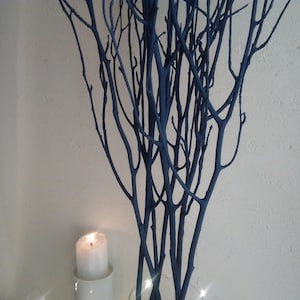 May include: A bunch of dark blue painted branches in a vase with a white candle in front of them.