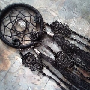 May include: Black dreamcatcher with black lace and beads. The dreamcatcher has a beaded cord and a crystal charm hanging from the center.