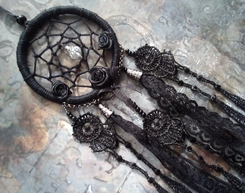 May include: Black dreamcatcher with black lace and beads. The dreamcatcher has a beaded cord and a crystal charm hanging from the center.