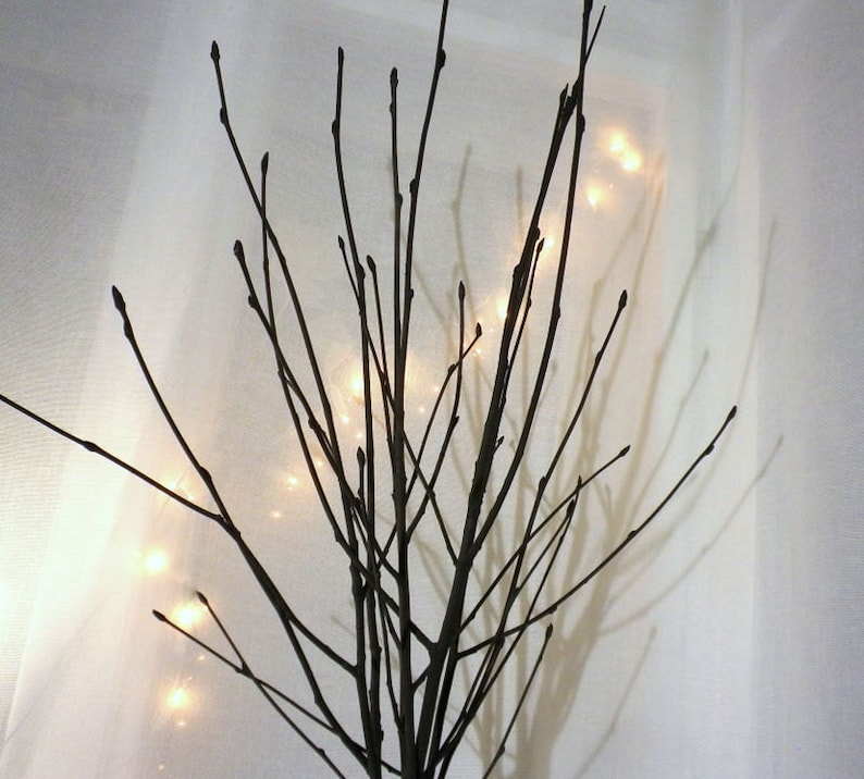 May include: A decorative branch arrangement with white lights strung throughout the branches. The branches are arranged in a vase or container, but the container is not visible in the image.