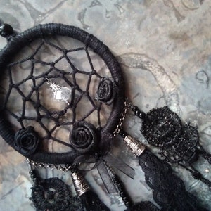 May include: Black dreamcatcher with a crystal charm and black fabric roses. The dreamcatcher has black lace trim and a black chain.