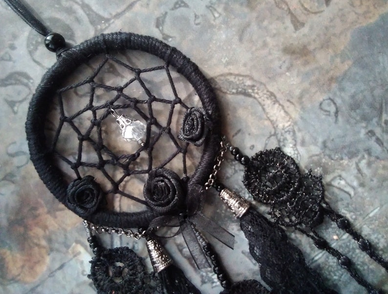 May include: Black dreamcatcher with a crystal charm and black fabric roses. The dreamcatcher has black lace trim and a black chain.