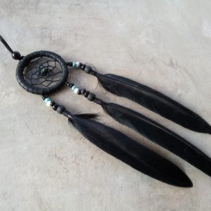 May include: A black dreamcatcher with a woven web design and three long black feathers. The dreamcatcher has small blue and black beads. A black cord is attached for hanging.