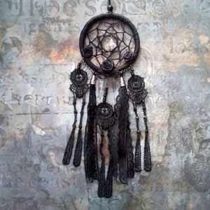 May include: Black dreamcatcher with black lace and beads hanging from it. The dreamcatcher has a web-like design and a small crystal in the center.