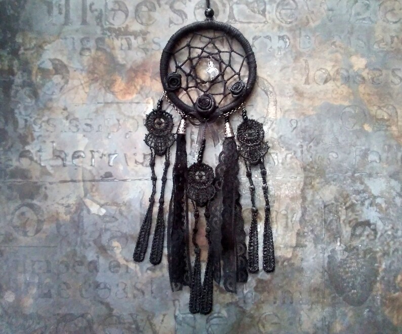 May include: Black dreamcatcher with black lace and beads hanging from it. The dreamcatcher has a web-like design and a small crystal in the center.