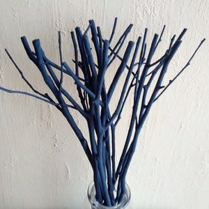 Peut inclure: Un bouquet de brindilles peintes en bleu fonc&eacute; dispos&eacute;es dans un vase. Les brindilles sont fines et ont un aspect naturel et rustique.