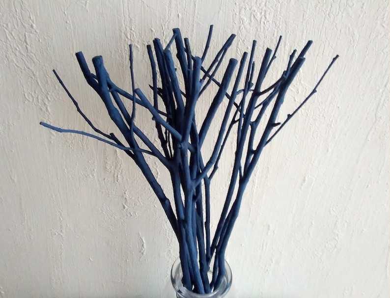Peut inclure: Un bouquet de brindilles peintes en bleu fonc&eacute; dispos&eacute;es dans un vase. Les brindilles sont fines et ont un aspect naturel et rustique.