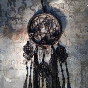 May include: Black dreamcatcher with black feathers and beads. The dreamcatcher has a black and white spiderweb design with a crystal in the center. There are three black roses on the dreamcatcher.