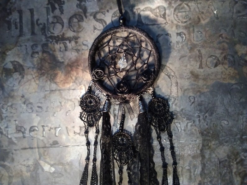 May include: Black dreamcatcher with black feathers and beads. The dreamcatcher has a black and white spiderweb design with a crystal in the center. There are three black roses on the dreamcatcher.