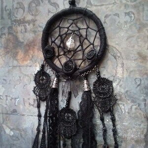 May include: Black dreamcatcher with a crystal bead and black lace tassels. The dreamcatcher has a black beaded border and three black fabric roses.