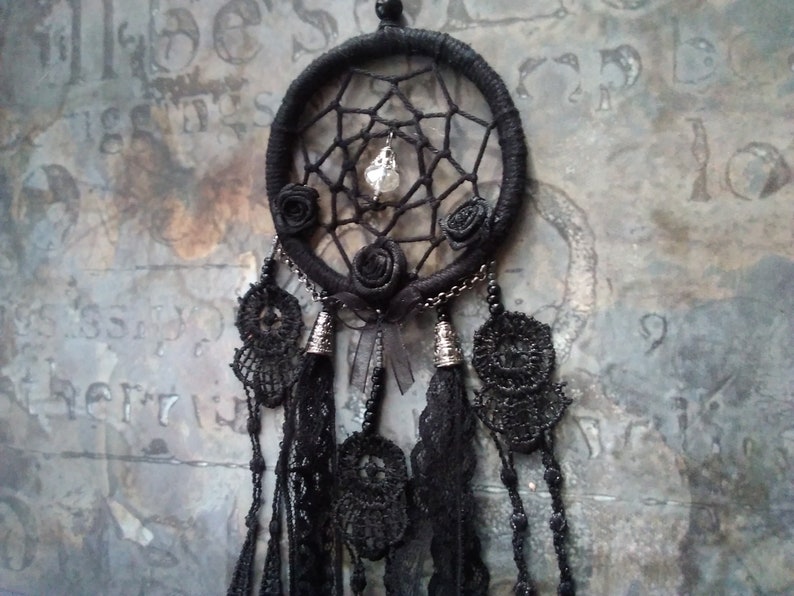 May include: Black dreamcatcher with a crystal bead and black lace tassels. The dreamcatcher has a black beaded border and three black fabric roses.