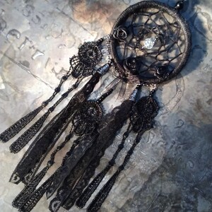 May include: Black dreamcatcher with black lace trim and beads. The dreamcatcher has a black and white spiderweb design with three black roses and a clear crystal bead in the center.