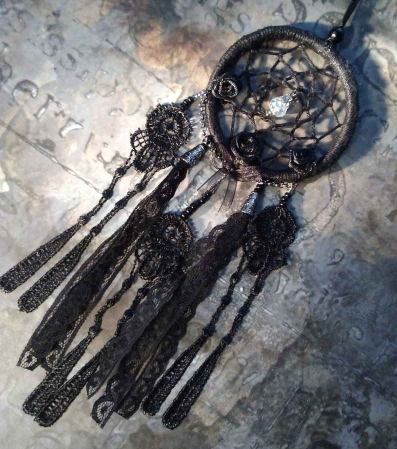 May include: Black dreamcatcher with black lace trim and beads. The dreamcatcher has a black and white spiderweb design with three black roses and a clear crystal bead in the center.