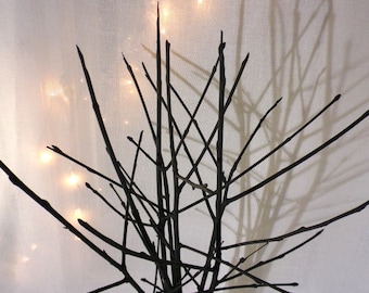 May include: A black twig tree sculpture with a white background. The twigs are arranged in a criss-cross pattern, creating a geometric design.