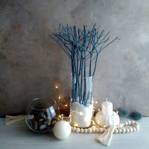 Peut inclure: Un vase en verre rempli de branches peintes en bleu et de sable blanc. Le vase est entour&eacute; de bougies blanches, d'une guirlande de lumi&egrave;res blanches et d'une guirlande de perles en bois.