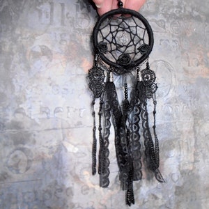 May include: Black dreamcatcher with black lace trim and black feathers. The dreamcatcher has a beaded chain and a crystal bead in the center.