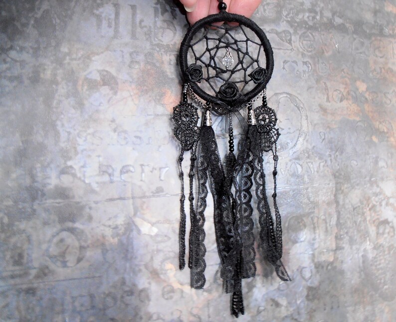 May include: Black dreamcatcher with black lace trim and black feathers. The dreamcatcher has a beaded chain and a crystal bead in the center.