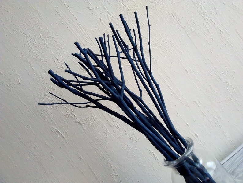 Peut inclure: Un bouquet de brindilles peintes en bleu fonc&eacute; dans un vase en verre transparent. Les brindilles sont dispos&eacute;es en &eacute;ventail.