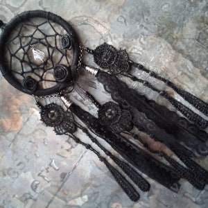 May include: Black dreamcatcher with a beaded fringe and three black roses. The dreamcatcher has a white crystal bead in the center.