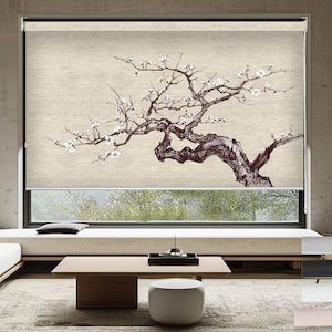 May include: A beige window shade with a black and white illustration of a blooming tree branch. The shade is partially rolled up, revealing a view of green foliage through a window.