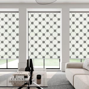 May include: Three white window shades with a black geometric pattern. The shades are pulled down and the pattern is visible. The shades are in a modern living room with a couch and a coffee table.
