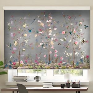 Puede incluir: Una cortina de ventana gris con un diseño floral que presenta tres árboles con flores rosas, blancas y moradas. Pájaros azules están posados en las ramas de los árboles. La cortina está bajada para revelar una ventana con un marco blanco.