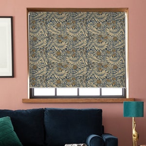 Puede incluir: Una persiana enrollable con un patrón floral repetido en tonos azul marino, beige y dorado. La persiana está instalada en un marco de ventana de madera. La habitación tiene una pared rosa, un sofá azul oscuro y una lámpara turquesa.