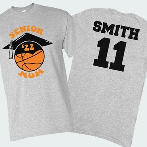 K&ouml;nnte beinhalten: Graues T-Shirt mit einem Basketball- und Abschlusskappen-Design, auf dem "Senior '22 Mom" steht. Auf der R&uuml;ckseite des Shirts steht der Name "Smith" und die Nummer "11" in Schwarz.