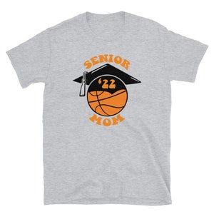 K&ouml;nnte beinhalten: Graues T-Shirt mit einem Basketball, auf dem eine Abschluss-Kappe sitzt. Der Basketball ist orange und schwarz. Der Text "Senior '22 Mom" ist auf das T-Shirt gedruckt.