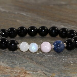 Pu&ograve; includere: Un braccialetto di pietre nere con perline di pietra di luna bianca, quarzo rosa e lapislazzuli blu.