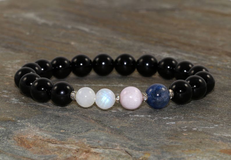 Pu&ograve; includere: Un braccialetto di pietre nere con perline di pietra di luna bianca, quarzo rosa e lapislazzuli blu.