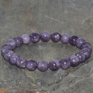 May include: A purple gemstone bracelet with round beads. The bracelet is made of natural stones and is approximately 8 inches in length.