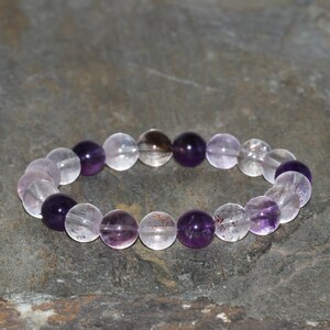Puede incluir: Un brazalete de cuentas de cristal morado y transparente con una mezcla de cuentas de amatista y cuarzo transparente.