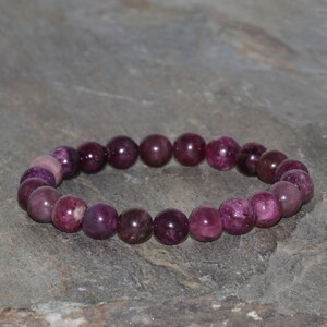 Könnte beinhalten: Ein Armband aus violetten Edelsteinen mit runden Perlen.