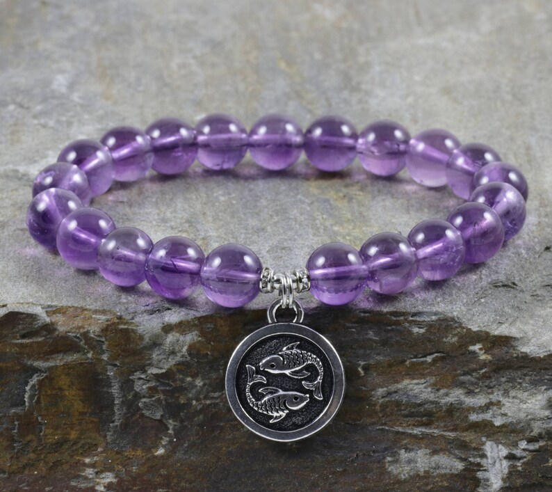 Puede incluir: Un brazalete de piedras preciosas de amatista p&uacute;rpura con un dije de plata que representa el s&iacute;mbolo astrol&oacute;gico de Piscis, dos peces.