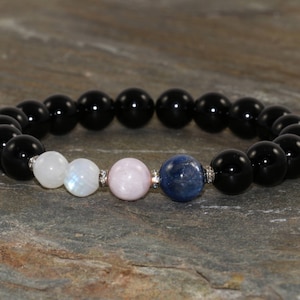Pu&ograve; includere: Un braccialetto di pietre nere con perline di pietra lunare, quarzo rosa e cianite blu.