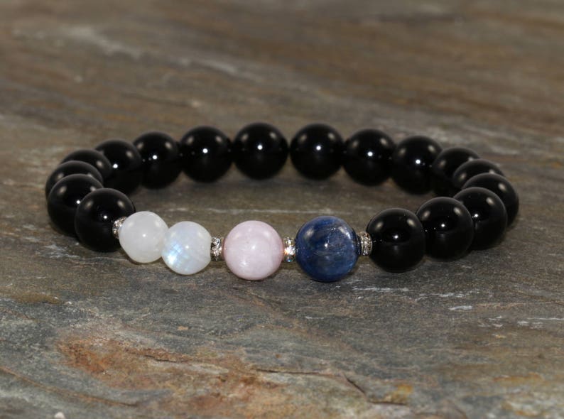 Pu&ograve; includere: Un braccialetto di pietre nere con perline di pietra lunare, quarzo rosa e cianite blu.