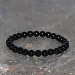 Puede incluir: Un brazalete negro hecho de cuentas redondas y lisas de ónix.