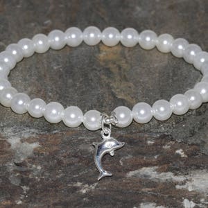 Peut inclure: Un bracelet en perles blanches avec un pendentif en forme de dauphin argenté. Le bracelet est composé de petites perles rondes et est enfilé sur une chaîne en argent.