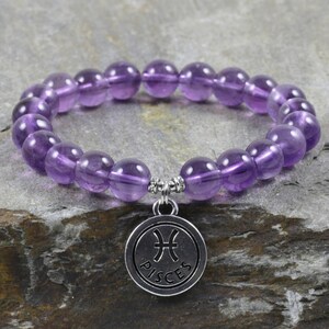 Puede incluir: Pulsera de piedras preciosas de amatista p&uacute;rpura con un dije de plata que dice "Piscis".