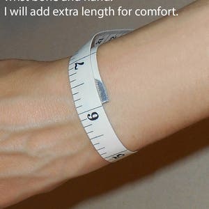 May include: A white measuring tape wrapped around a person's wrist to show how to measure for a bracelet. The tape reads 6, 7, 8, 9, and 10 inches. The text above the wrist reads "Measure around the wrist between the wrist bone and hand. I will add extra length for comfort."