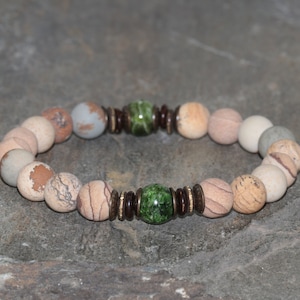 Puede incluir: Un brazalete de cuentas de piedra marrón y beige con dos cuentas de piedra preciosa verde y cuentas de madera marrón.