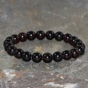 Puede incluir: Un brazalete de piedras negras con cuentas redondas. El brazalete está hecho de piedras de granate rojo oscuro.