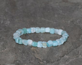 Puede incluir: Un brazalete de piedras preciosas azul claro hecho de pequeñas cuentas cuadradas. El brazalete está hecho de piedras naturales y tiene un diseño simple y elegante.