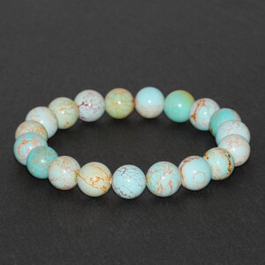 May include: A turquoise and brown beaded bracelet with a round shape. The beads are made of a natural stone with a marbled pattern.