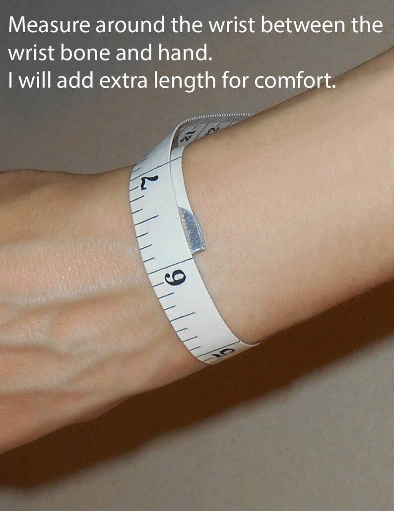 Pu&ograve; includere: Un nastro di misura bianco avvolto attorno al polso di una persona, che mostra una misura di 9 pollici. Il testo "Measure around the wrist between the wrist bone and hand. I will add extra length for comfort." &egrave; visibile sopra il polso.