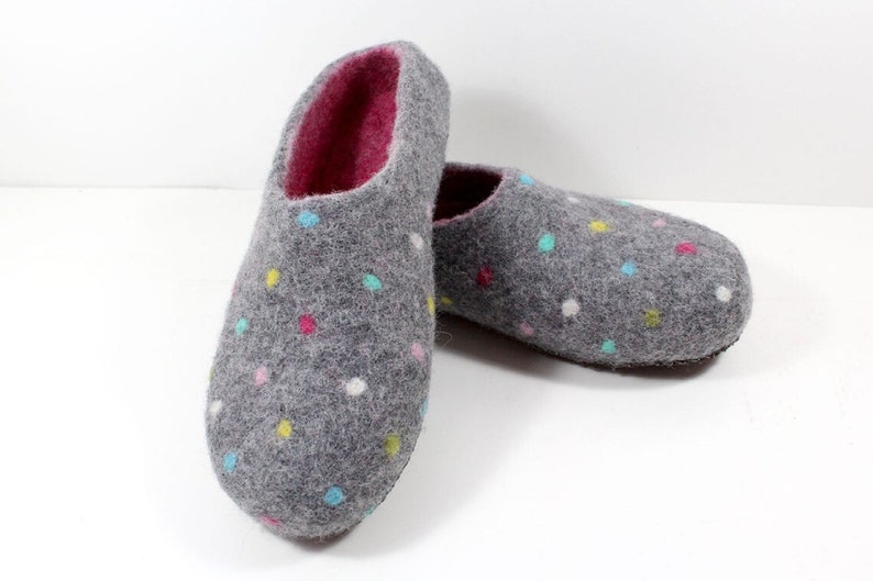 May include: A pair of gray felt slippers with a colorful polka dot pattern. The slippers have a pink lining and a closed toe.