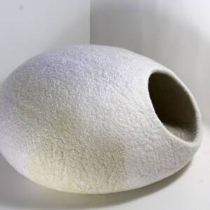 May include: A white felt cat bed shaped like an egg with a large opening on one side. The bed is made of a soft, fluffy material and is perfect for cats to curl up in.